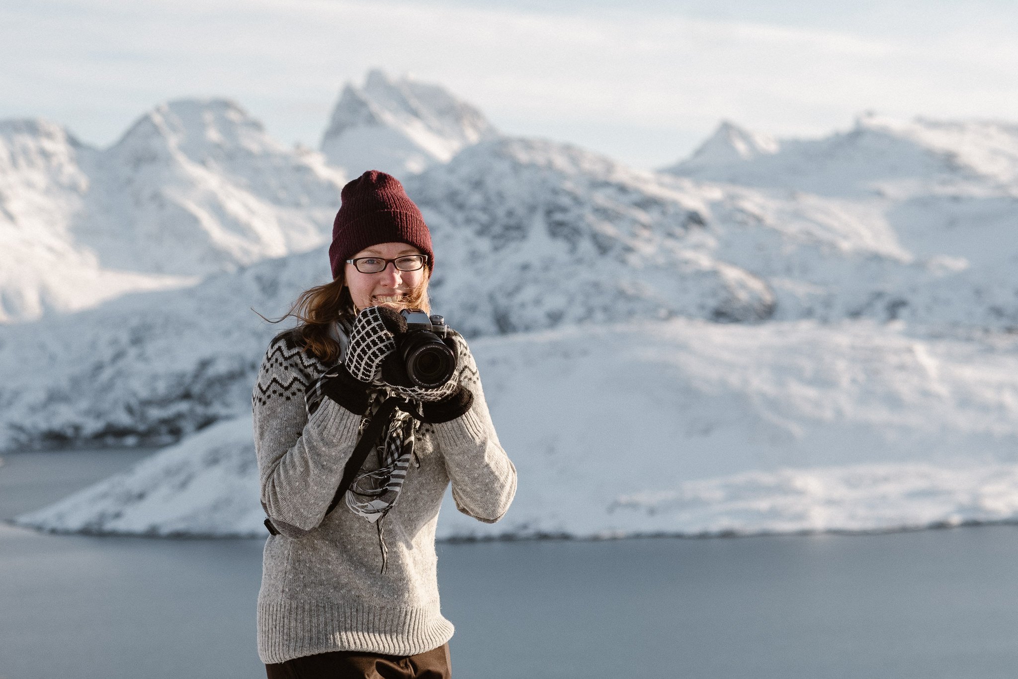 Norway elopement photographer Nina Larsen Reed, a woman holding a camera in front of snow-covered mountains in Lofoten