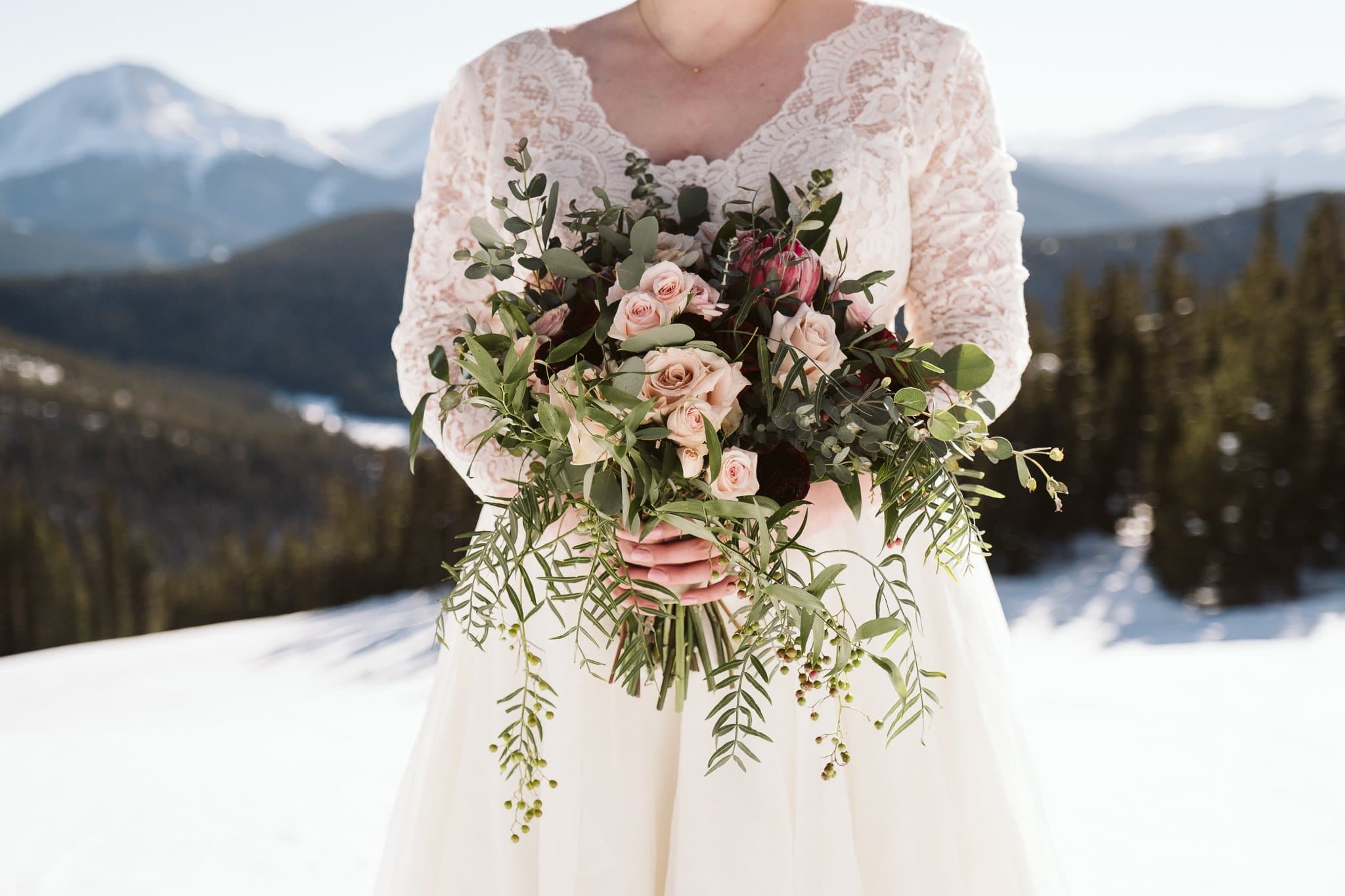 Bride with long sleeve lace wedding dress at winter wedding, holding modern green bouquet with pink and purple flowers.