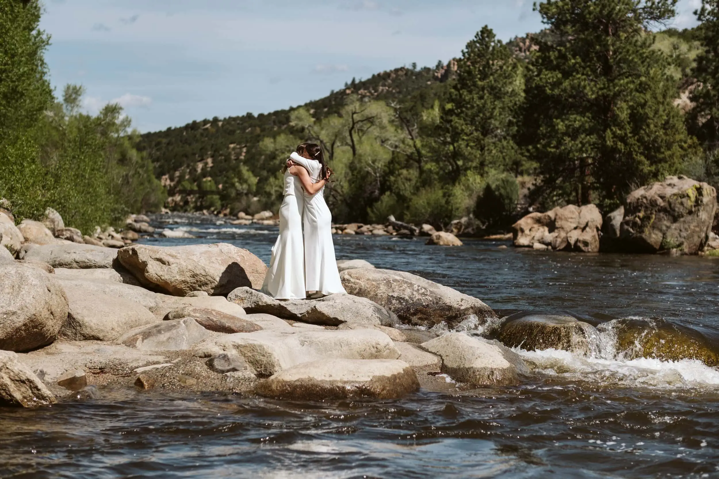 Two brides hug on the banks of the Arkansas River outside the Surf Hotel in Buena Vista